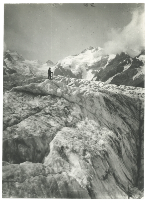 Das Schwarzweißfoto zeigt einen schwarz gekleideten Mann mit Gehstock steht auf einem Gletscher.